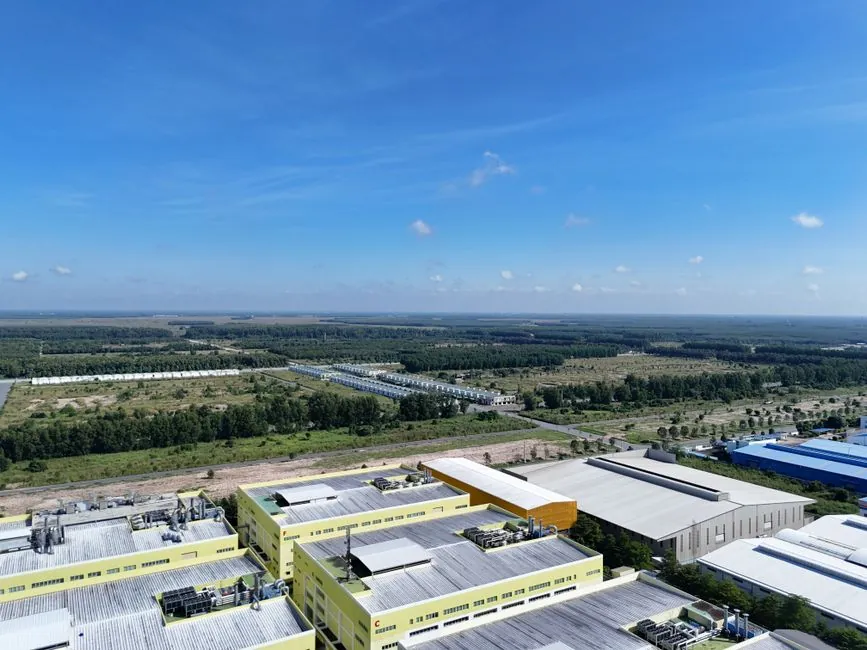 Aerial view of industrial buildings and expansive green landscape under a clear blue sky in Thủ Dầu Một, Vietnam.