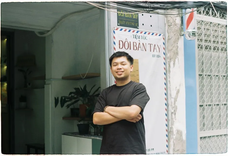 Smiling barber standing confidently at the entrance of a Vietnamese hair salon.