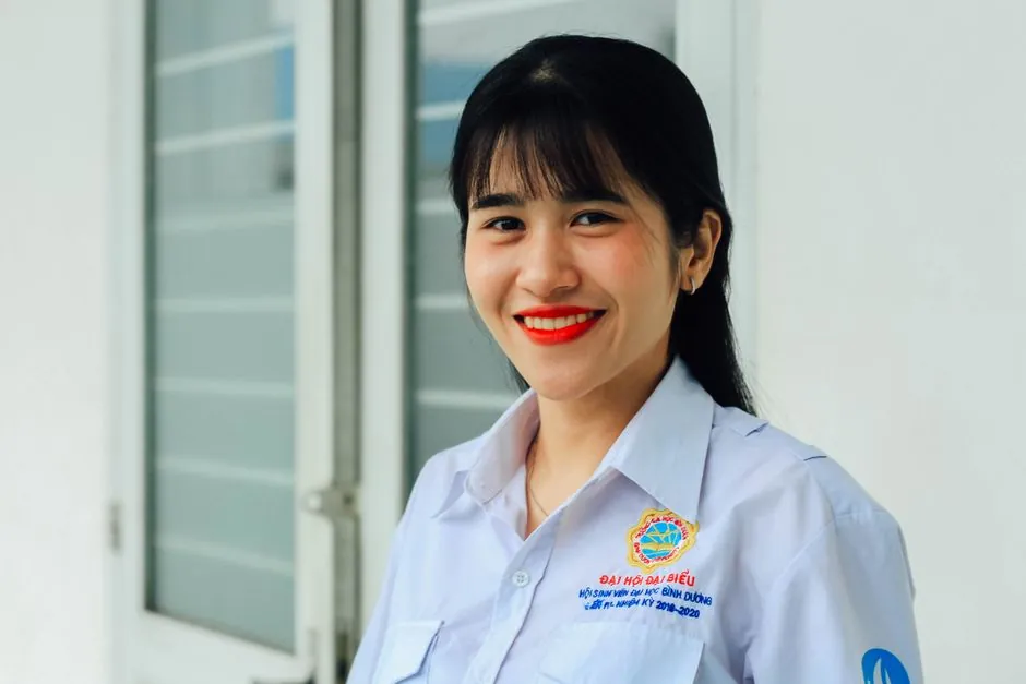 Portrait of a smiling woman in a white shirt standing indoors, exuding confidence.
