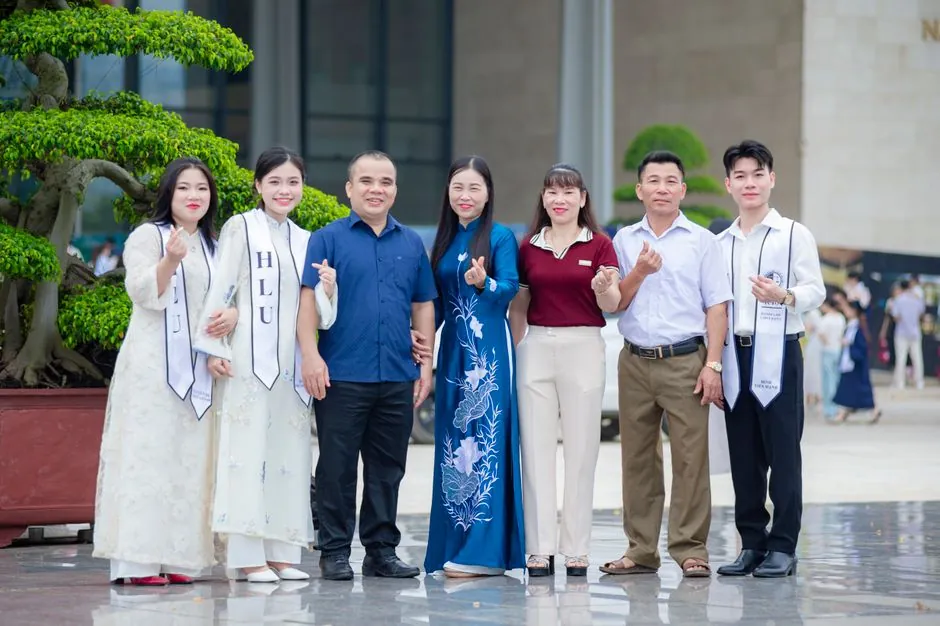 Group of adults in graduation attire posing outside Hanoi Law University, Vietnam.