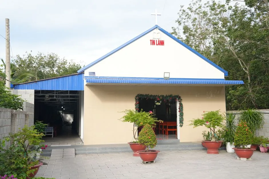 A small rural church with a blue roof, decorated entrance and potted plants.